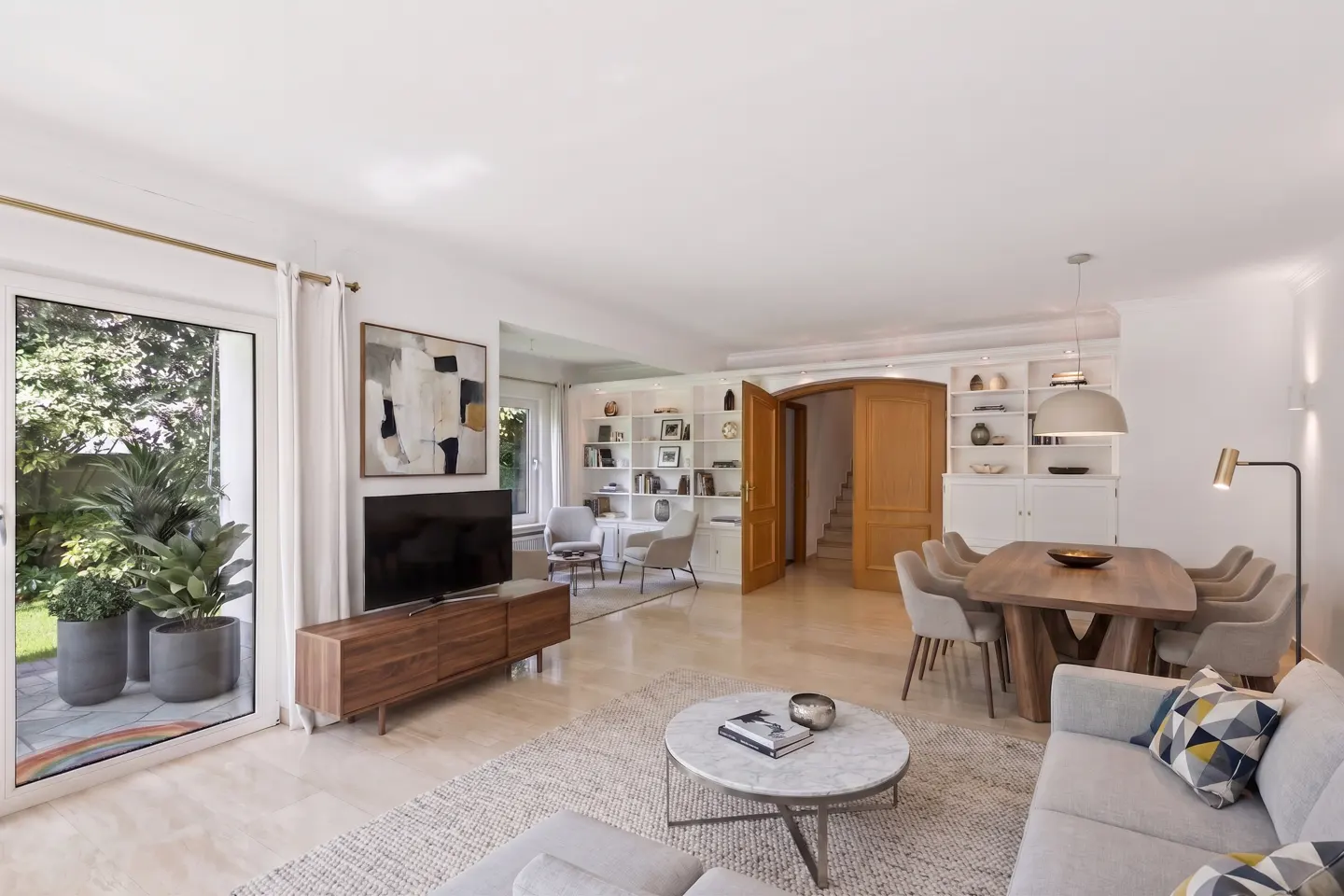Bright, open-plan living room with a dining area, modern furniture, marble coffee table, and a view of a patio garden.