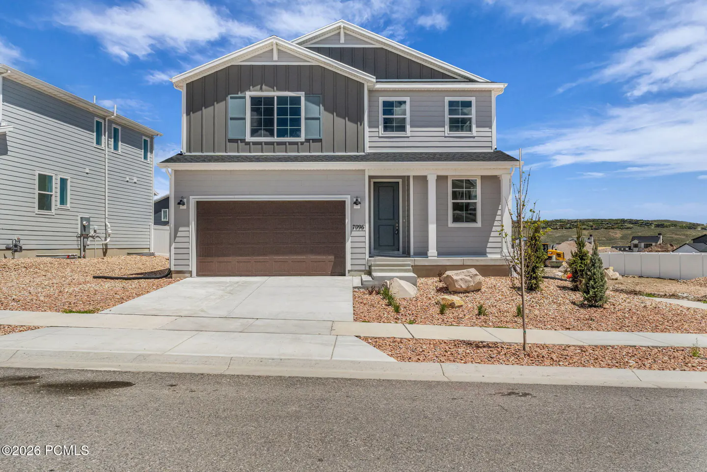 Two-story house with gray siding, brown garage door, and blue shutters under a blue sky.
