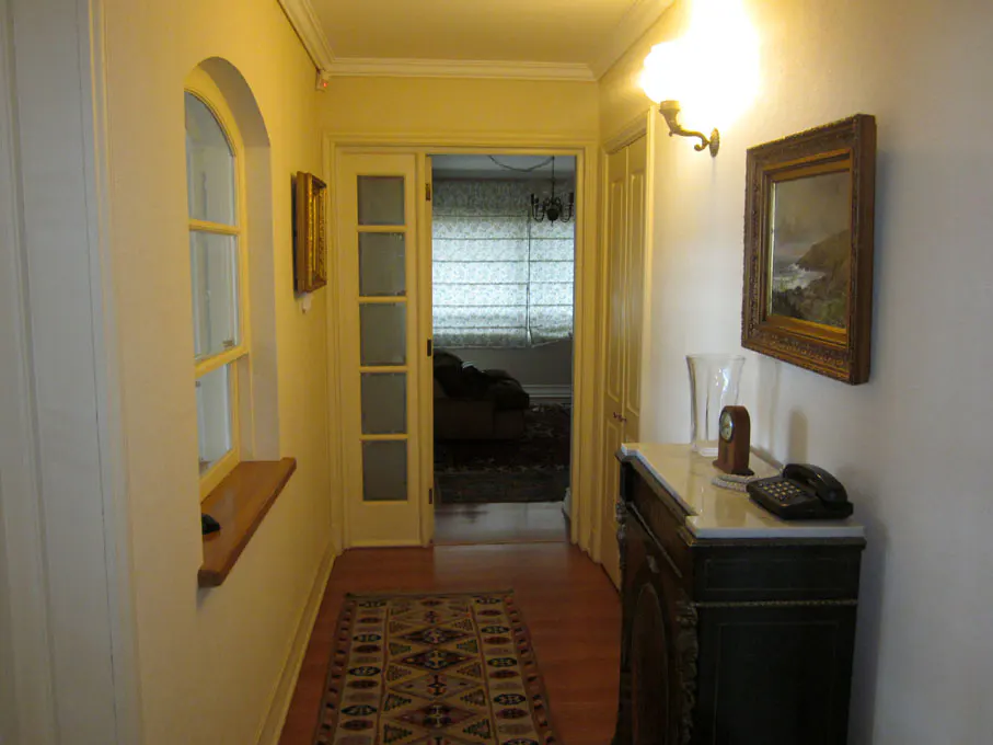 Hallway with arched window, patterned rug, and dark wood cabinet with marble top. A framed landscape painting hangs on the wall.