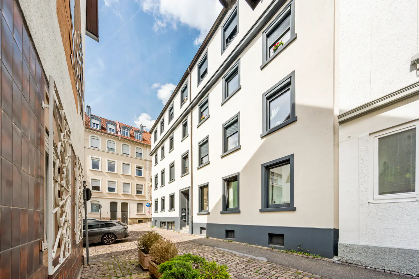 Exterior view of a multi-story apartment building with white walls and dark gray window frames on a cobblestone street.