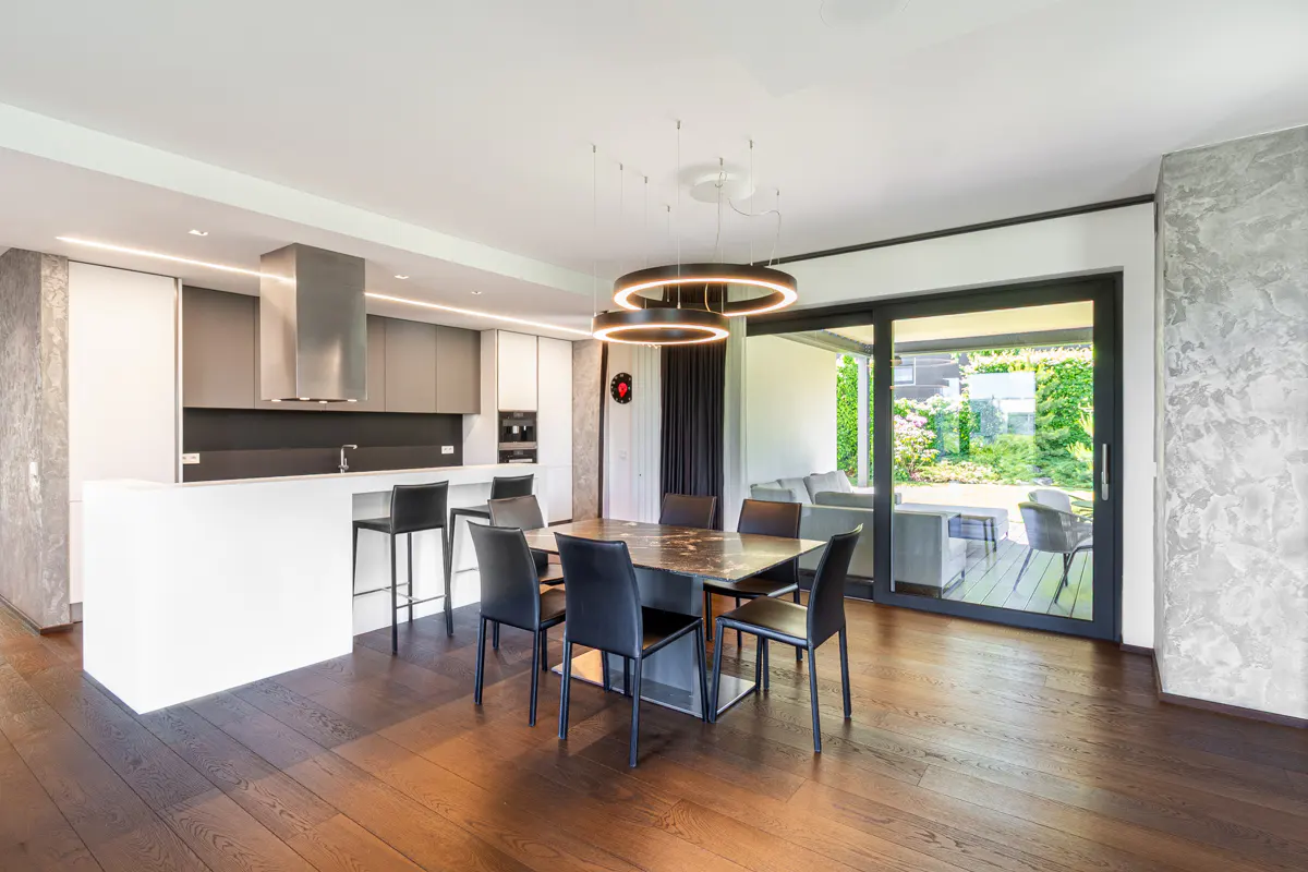 A modern, open-concept kitchen and dining area with dark wood floors, a marble table with black chairs, and a view of the outdoor patio.