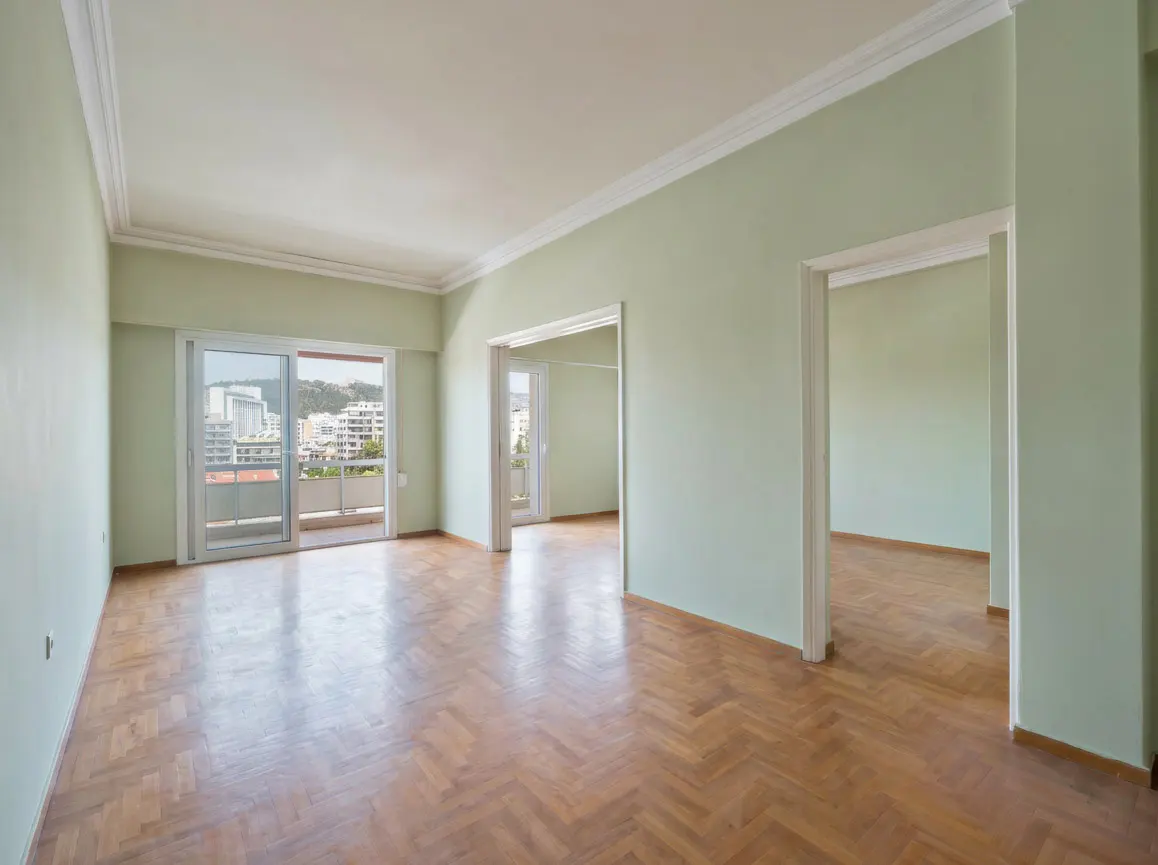 Empty room with light green walls, herringbone wood floor, and balcony doors with a city view.