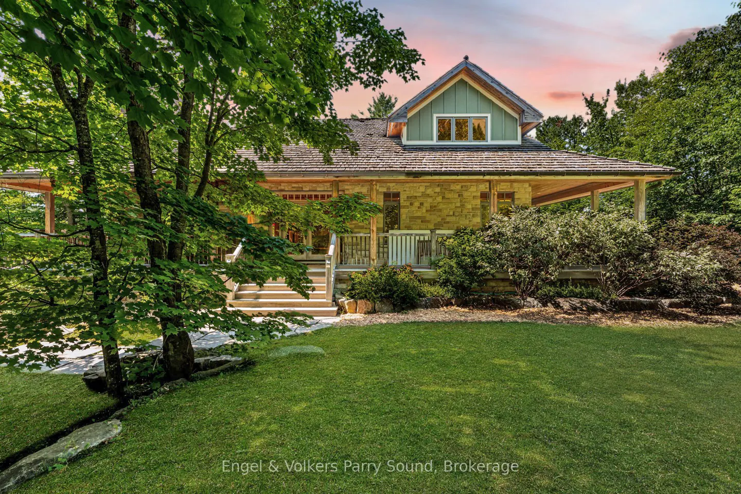 A single-story house with a porch, stone facade, and green gable sits on a green lawn with trees.
