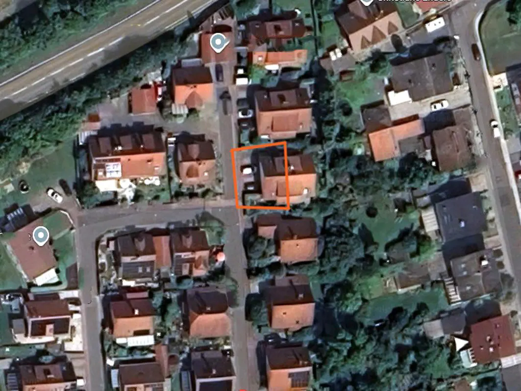 Aerial view of a residential area with houses, trees, and roads. The house of interest is highlighted with an orange square.
