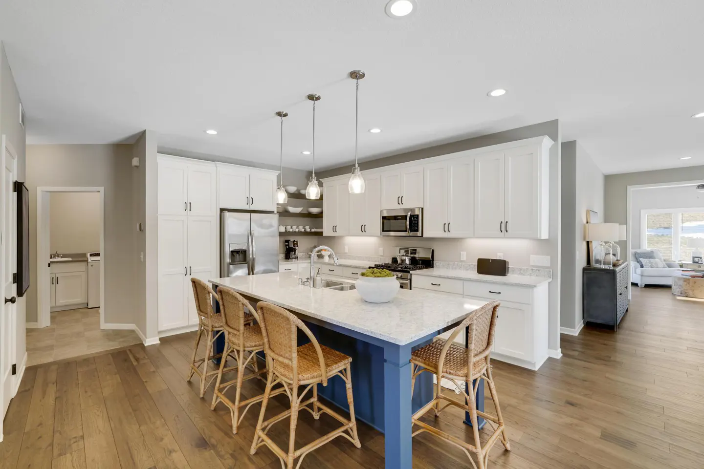 A modern kitchen with white cabinets, stainless steel appliances, and a blue island with wicker stools.