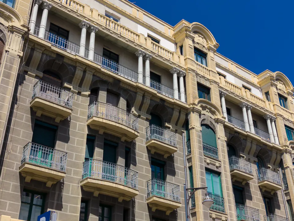 Exterior view of a multi-story building with balconies, stone facade, and architectural details under a clear blue sky.