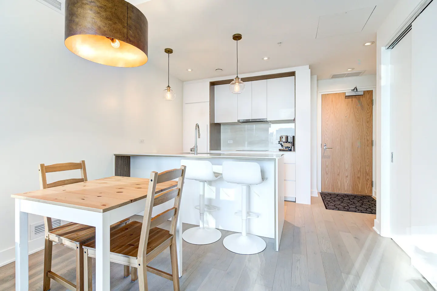 Modern kitchen with white cabinets, breakfast bar with two stools, and a wooden dining table with chairs.
