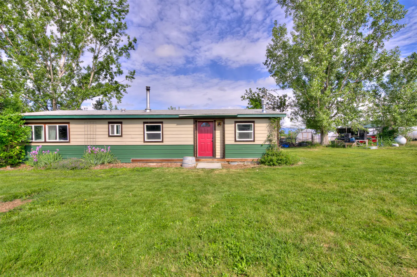 Single-story home with tan and green siding, a bright red front door, and a large grassy yard under a blue sky.