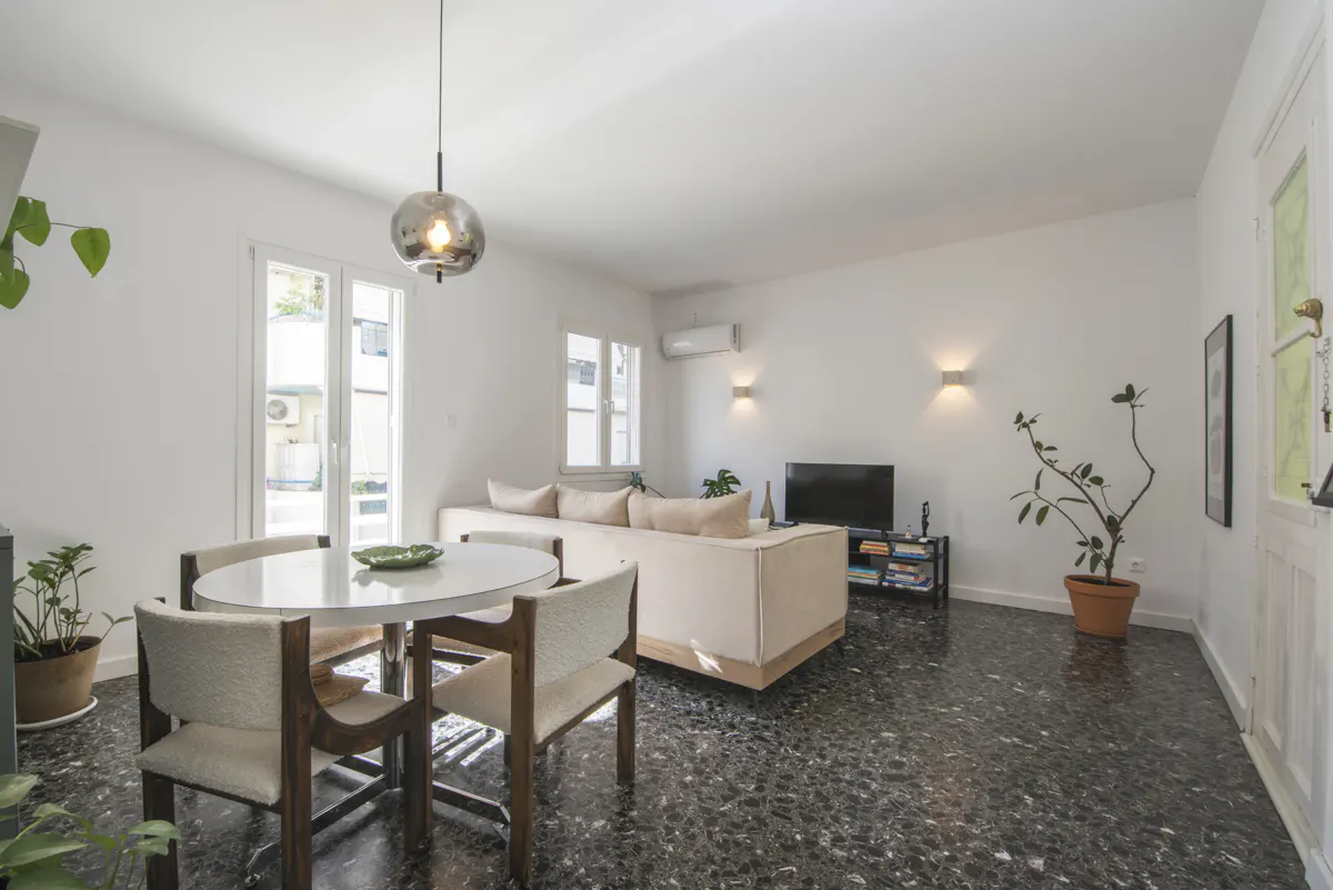 Bright living room with white walls, black speckled floor, round table, beige sofa, and a modern pendant light.