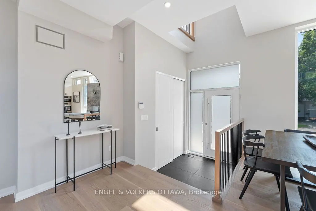 Bright entryway with light wood floors, white walls, and a tall arched mirror above a marble-topped console table. A white door and a dining table are also visible.