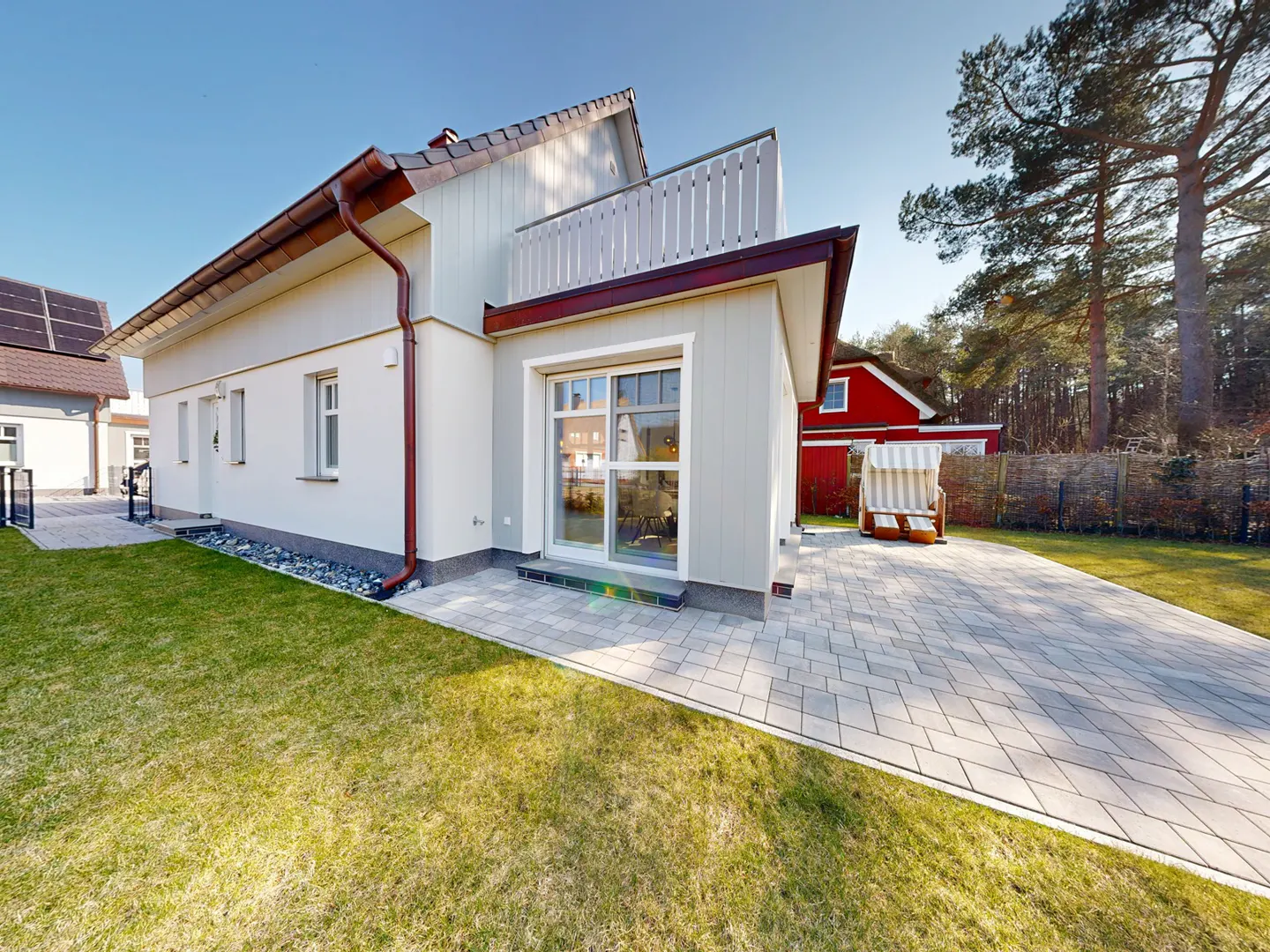 Exterior view of a modern, light gray house with a brown roof and trim, a small balcony, and a paved patio.