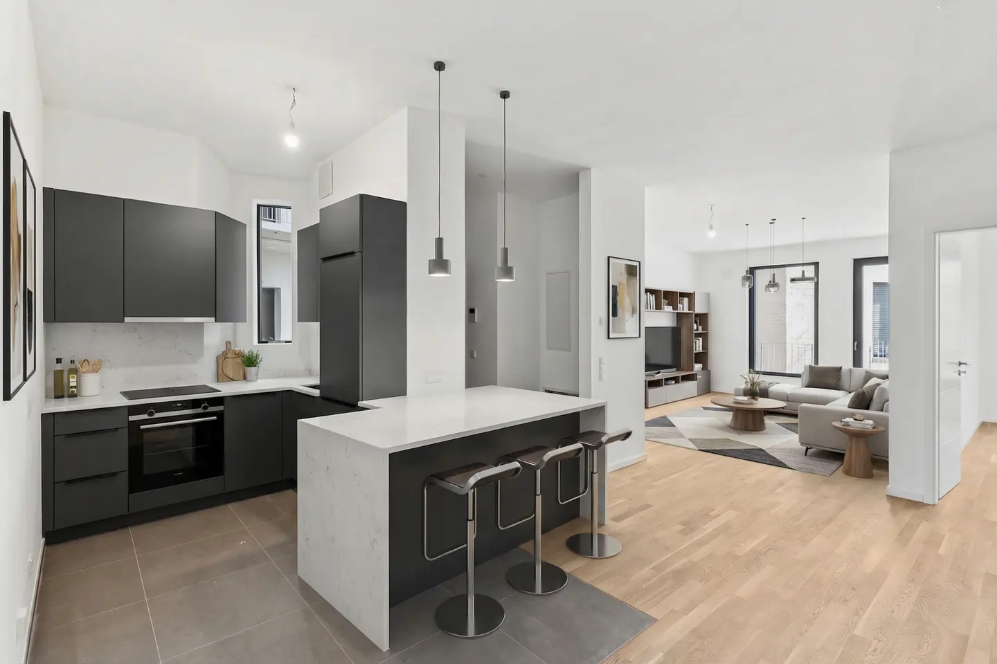 Open-concept living space with gray kitchen cabinets, white countertops, island with stools, and a living room with a gray sofa.