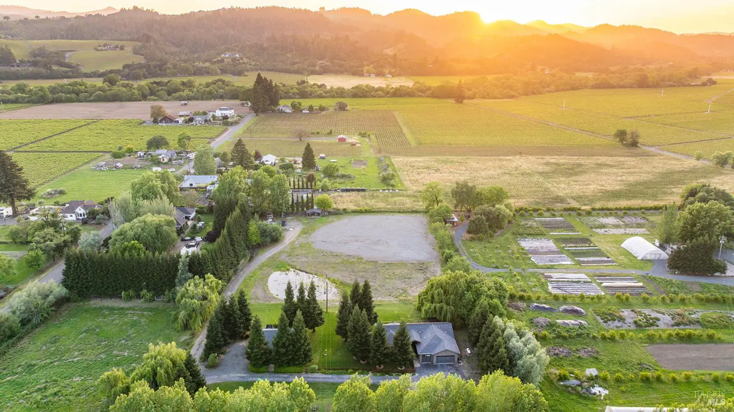 Aerial view of a rural property at sunset, featuring a house, fields, and distant mountains.