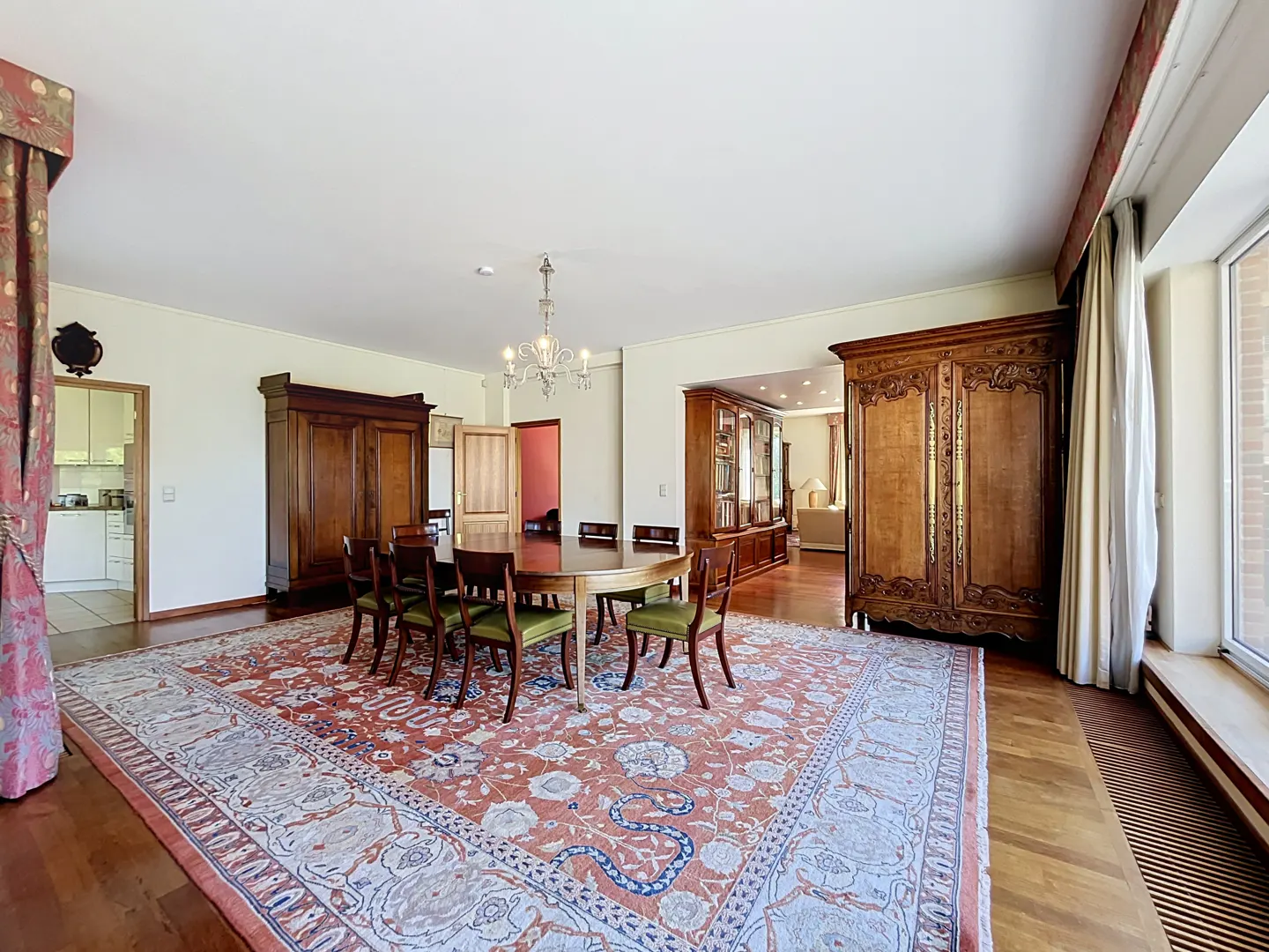Formal dining room with an oval wooden table, green chairs, large antique cabinets, and a patterned red area rug.