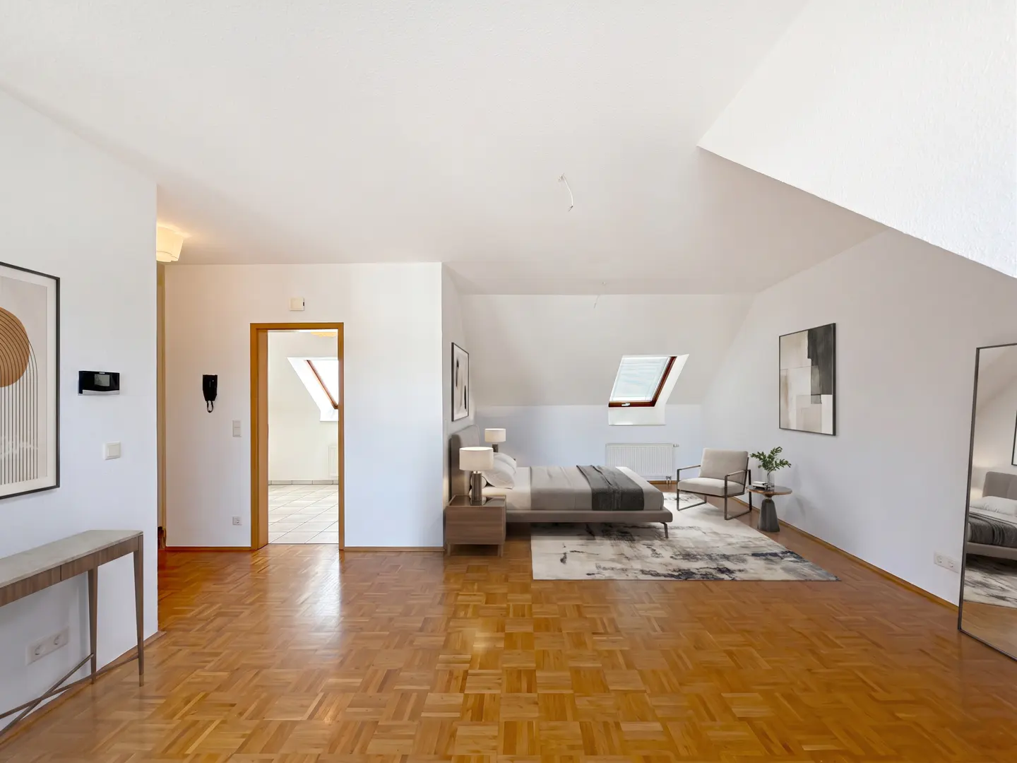 Bright, airy bedroom with wood floors, white walls, and a skylight. A bed, chair, and artwork decorate the space.