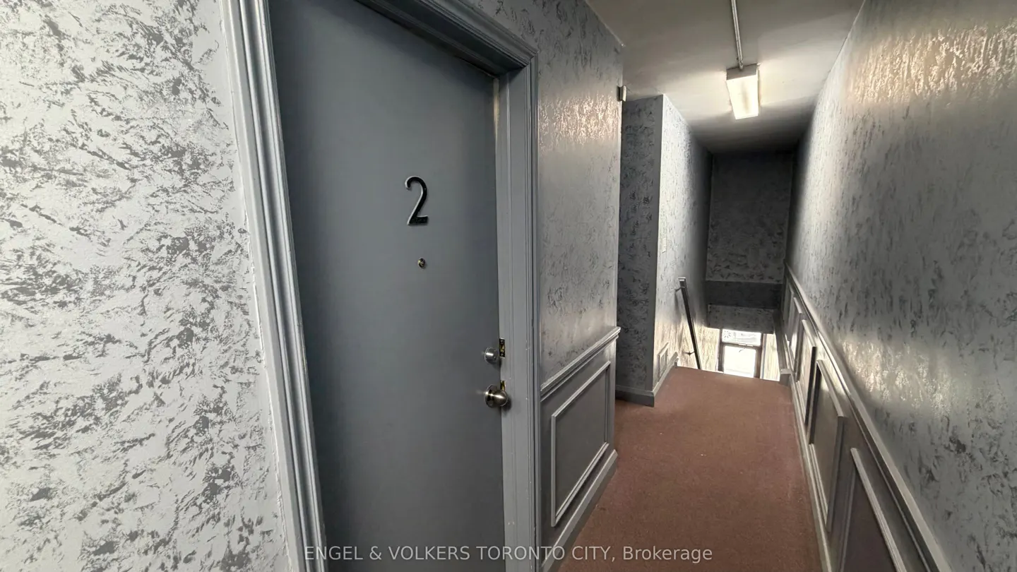 Hallway with gray walls and a door labeled "2". A staircase leads down, lit by a fluorescent light.