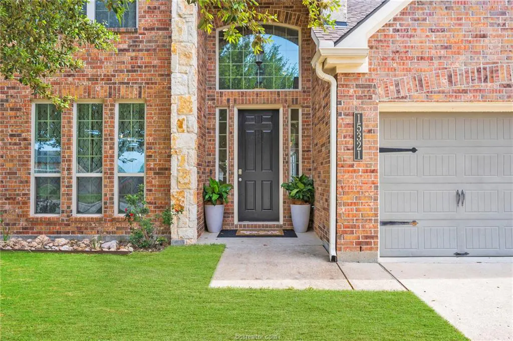 Brick house exterior with a black front door, stone accents, and a two-car garage. Green lawn and plants add curb appeal.