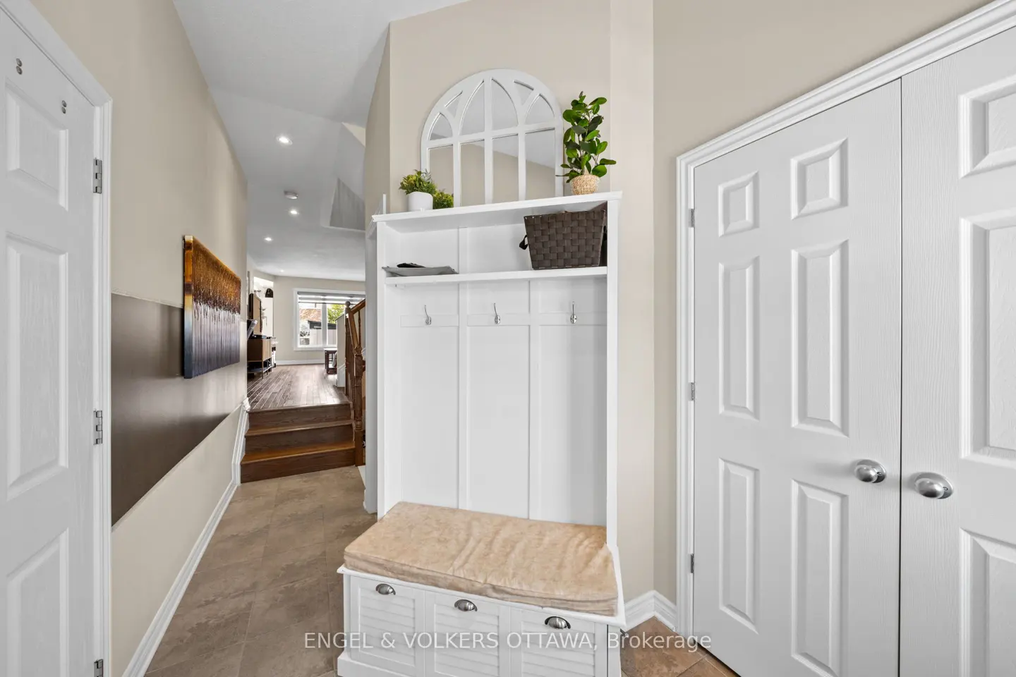 Entryway with white hall tree, bench, and storage. A painting hangs on the wall, and a staircase leads to the next level.