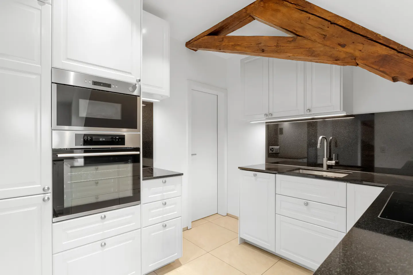 Bright kitchen with white cabinets, black granite countertops, and stainless steel appliances. A wooden beam is visible on the ceiling.