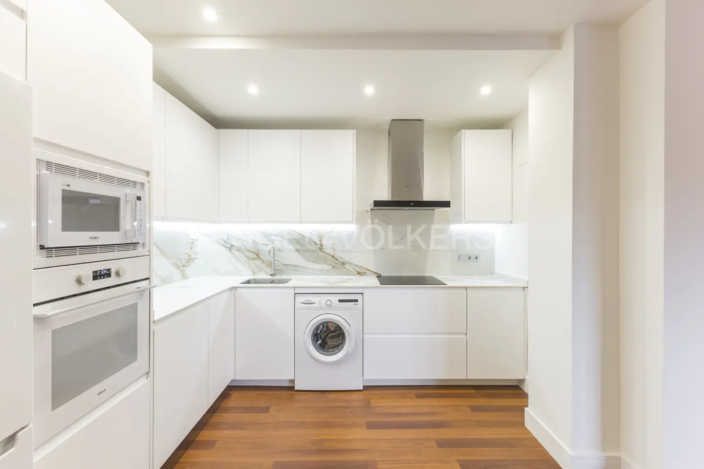 Bright, modern kitchen with white cabinets, marble backsplash, and wood floors. Appliances include a microwave, oven, and washing machine.