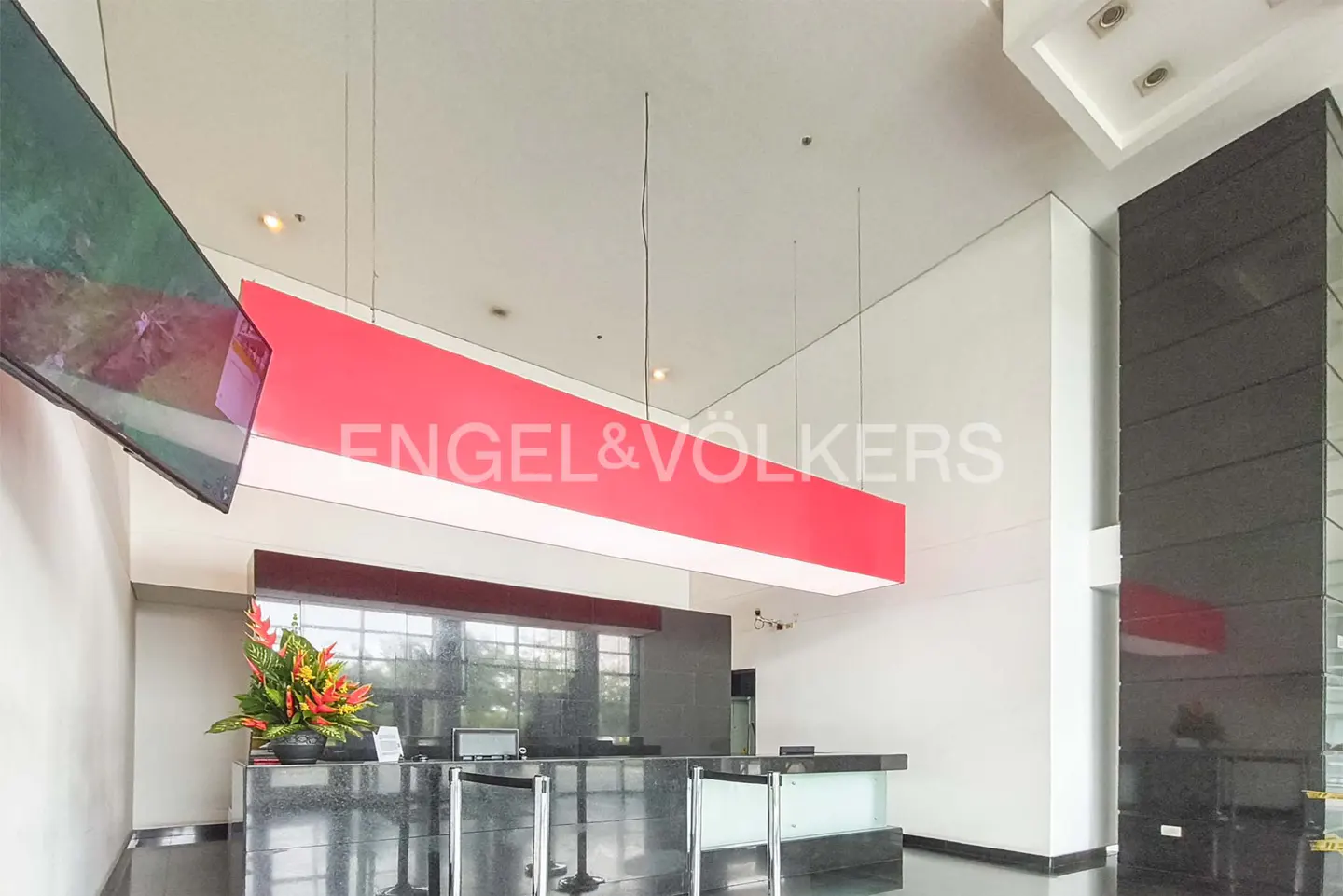 Lobby view with a black marble reception desk, floral arrangement, and a red Engel & Völkers sign hanging from the ceiling.