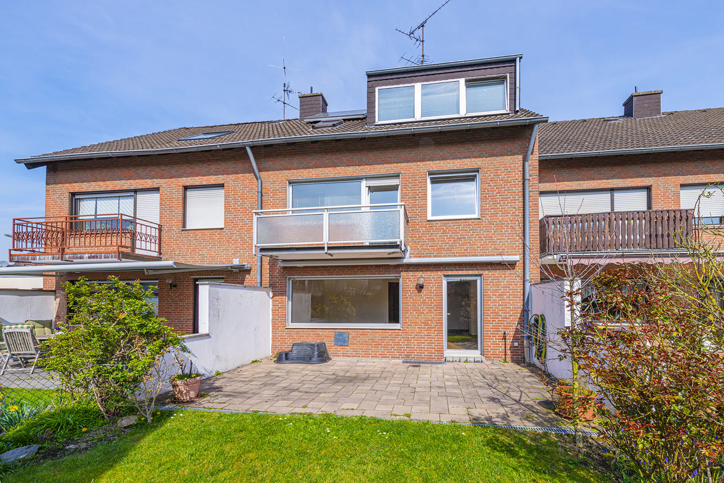 Exterior view of a three-story red brick townhouse with balconies and a stone patio.