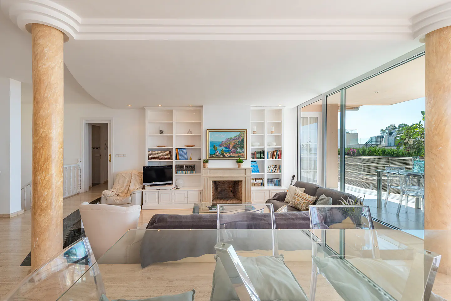 Bright living room with marble columns, white built-in shelves, fireplace, and sliding glass doors to a balcony.