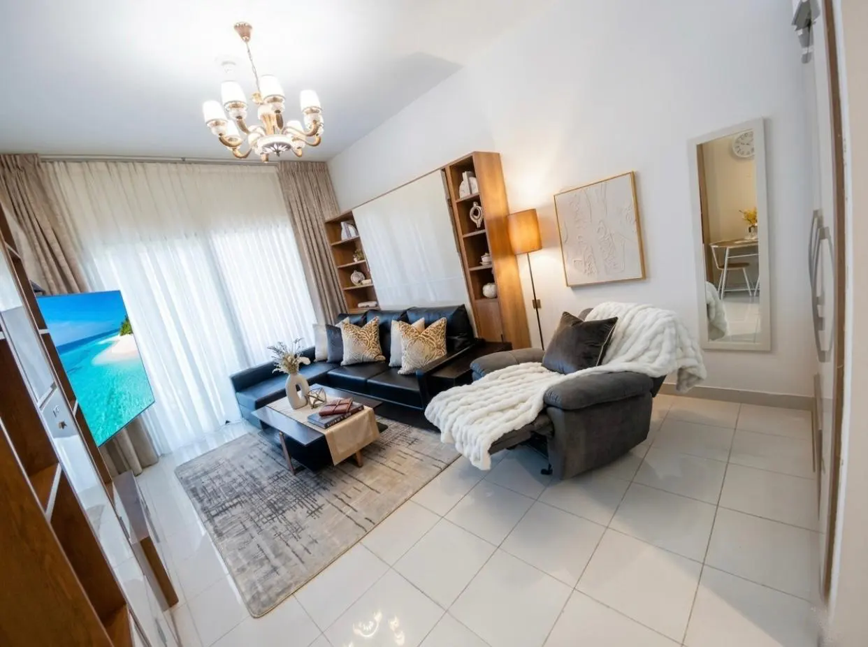 Living room with a black leather sofa, gray recliner with a white blanket, and a TV showing a beach scene.