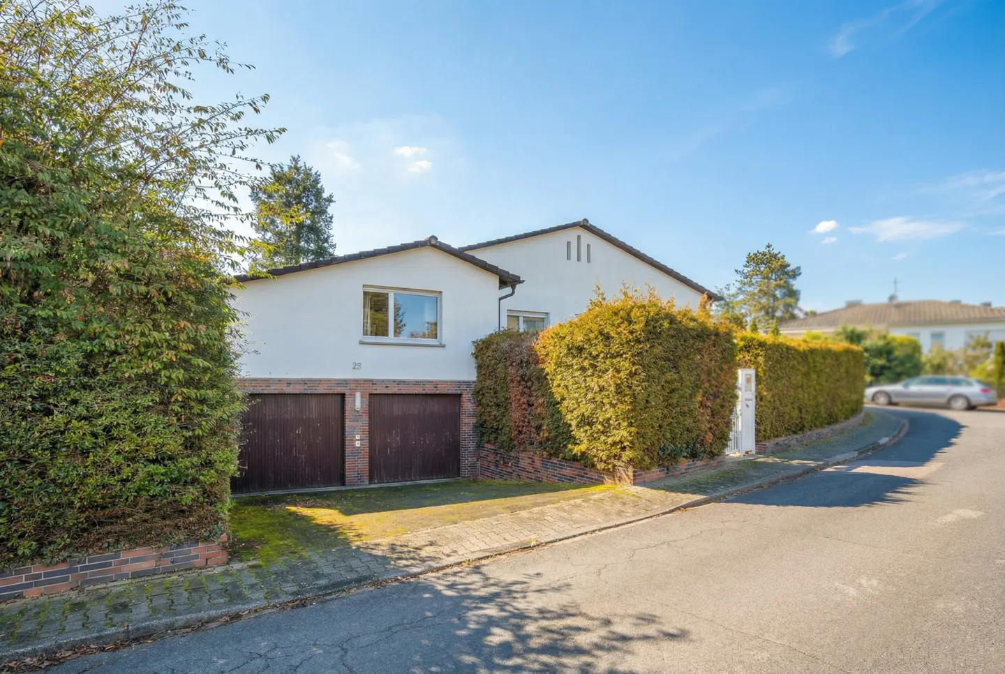 A white house with brown garage doors is surrounded by green bushes on a sunny day.