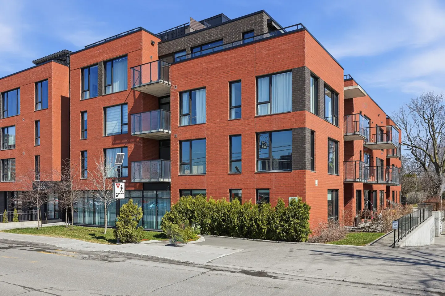 Modern red brick apartment building with black framed windows and glass balconies on a sunny day.