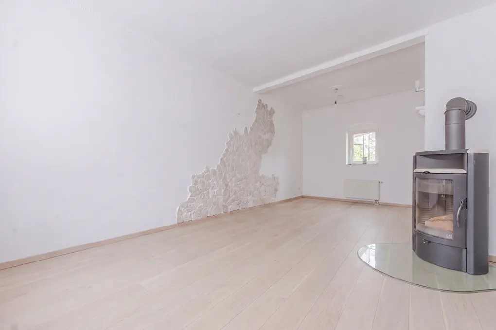 Bright, empty room with light wood floors, white walls, and a modern black fireplace on a glass base. A textured design is on the left wall.