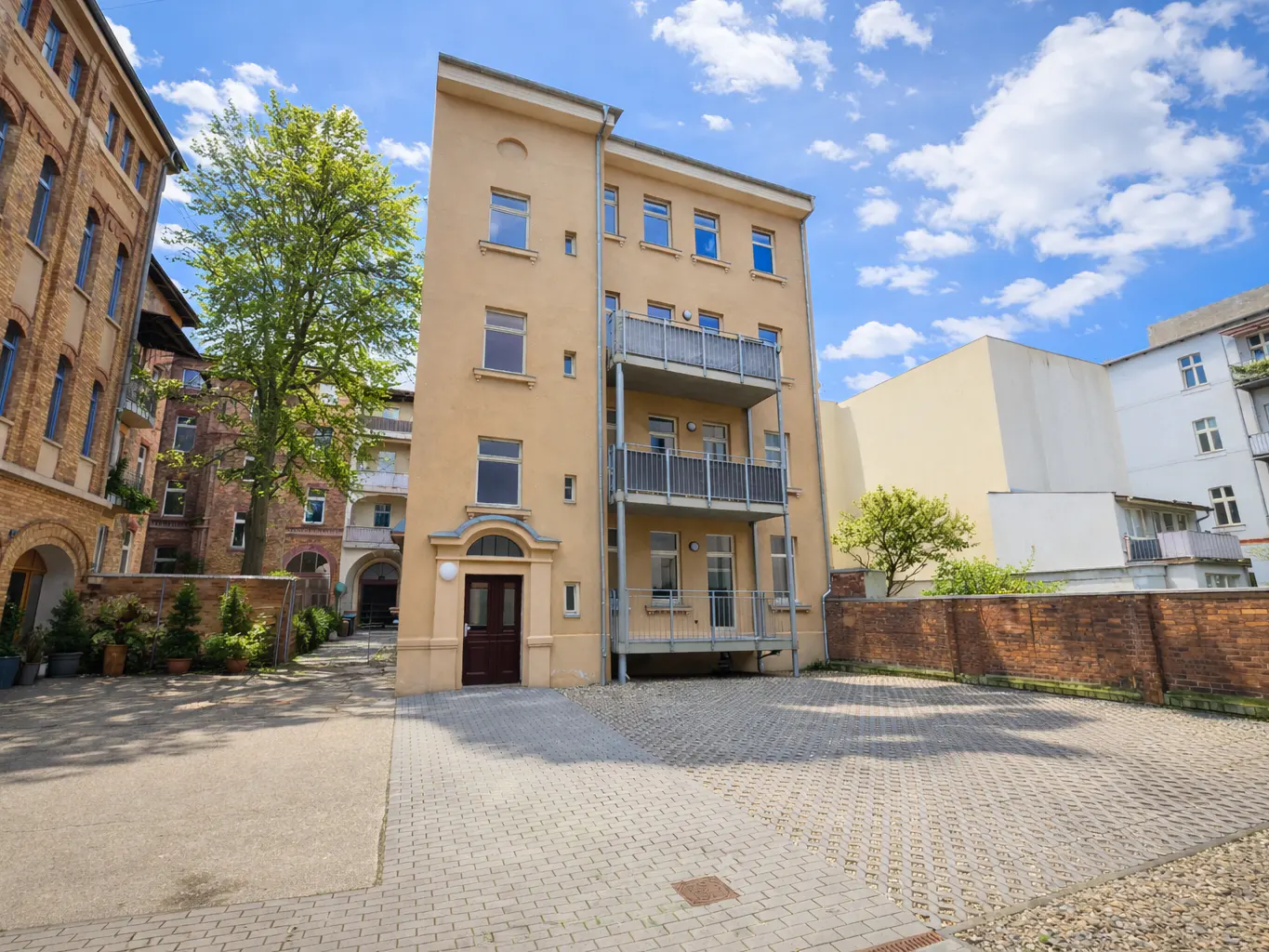 A tan apartment building with two balconies and a brown door, set against a blue sky with white clouds.