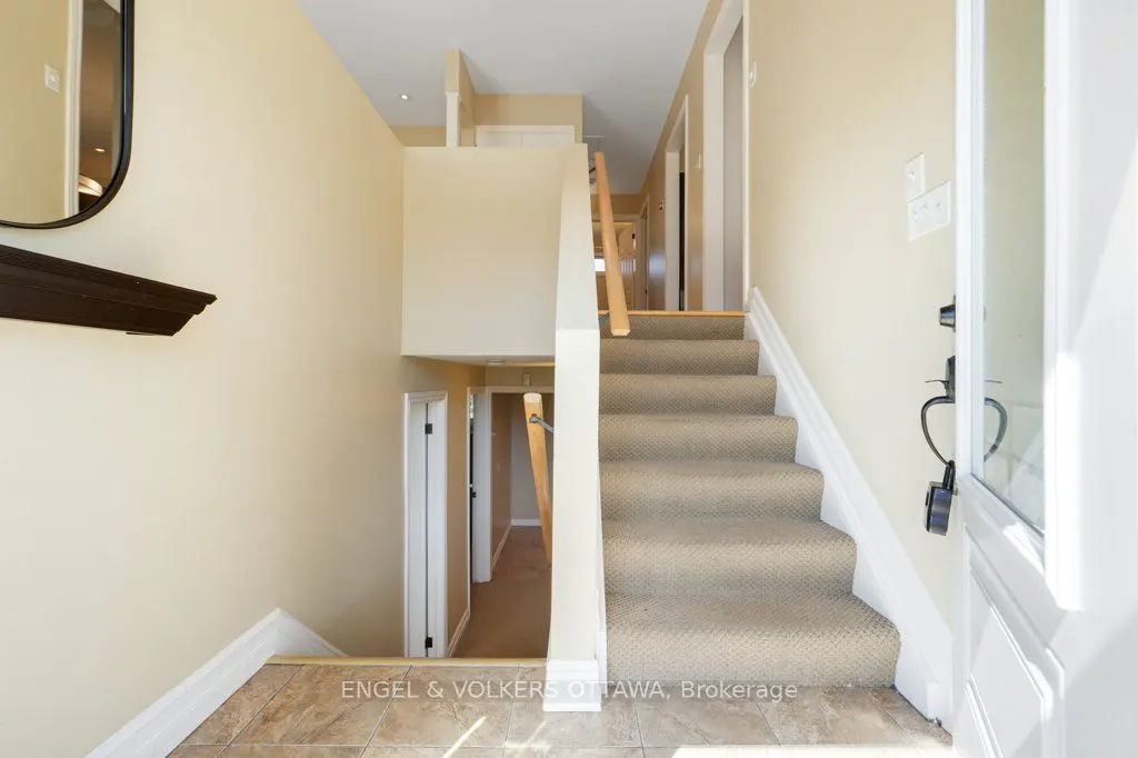 Entryway with beige walls, carpeted stairs, and a white door ajar. A dark wood shelf and mirror are on the left wall.