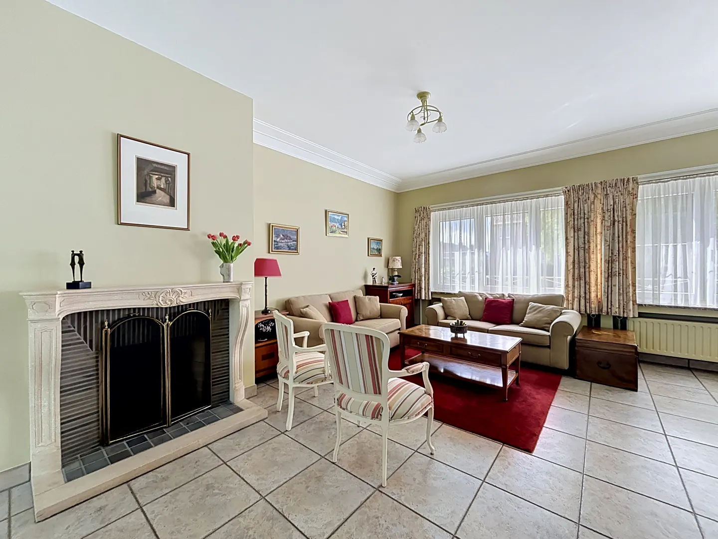 Living room with a stone fireplace, two striped armchairs, beige sofas, a wooden coffee table, and a red area rug.