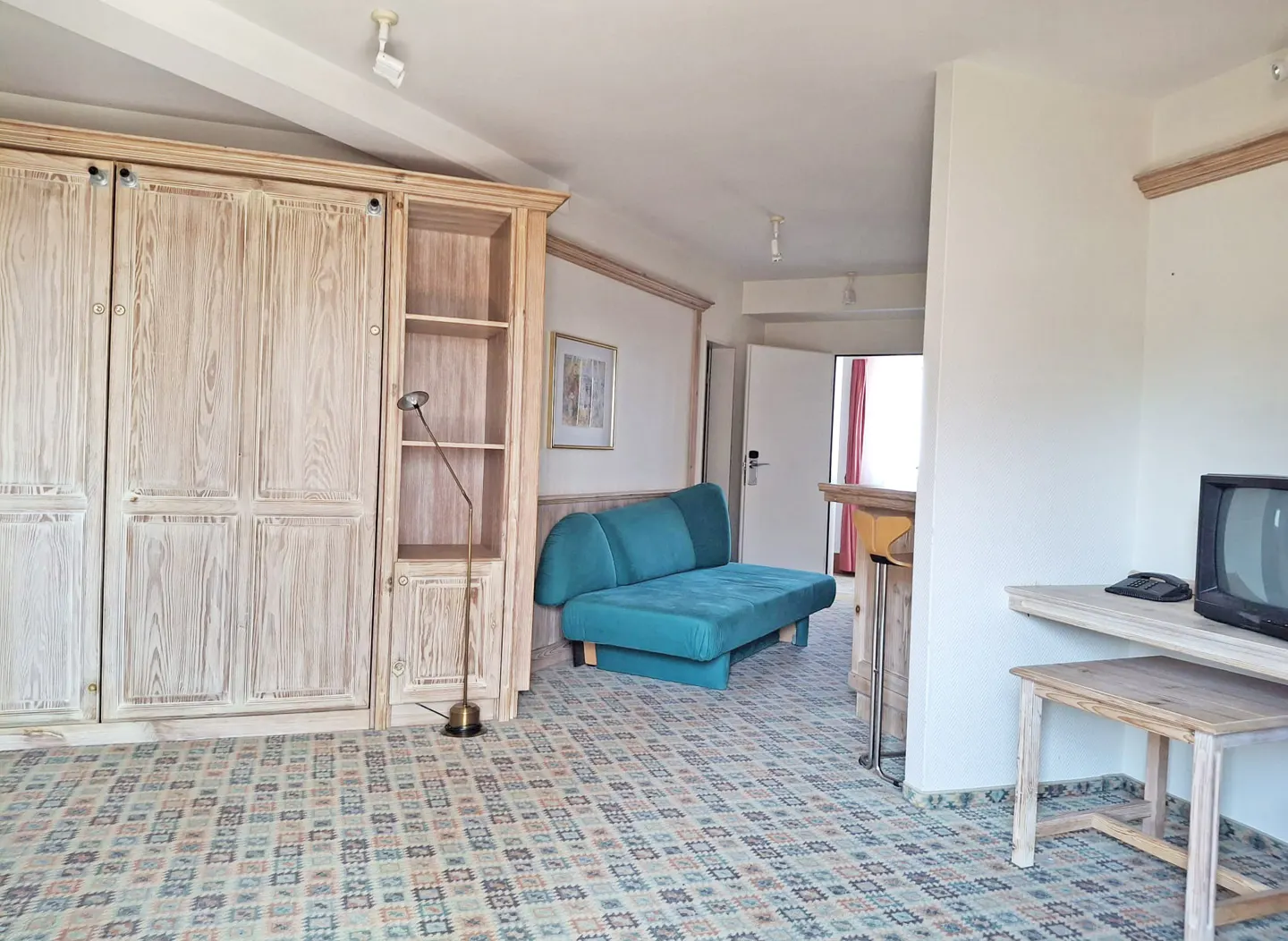 A bright room with a large wooden cabinet, a teal sofa, and a vintage television.