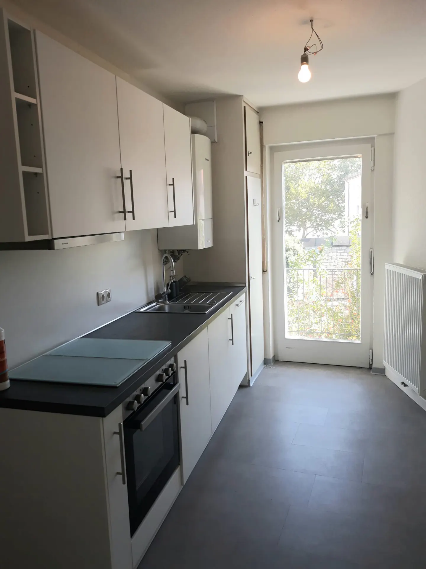 Modern kitchen with white cabinets, dark countertops, built-in oven, and a glass door leading to a balcony.