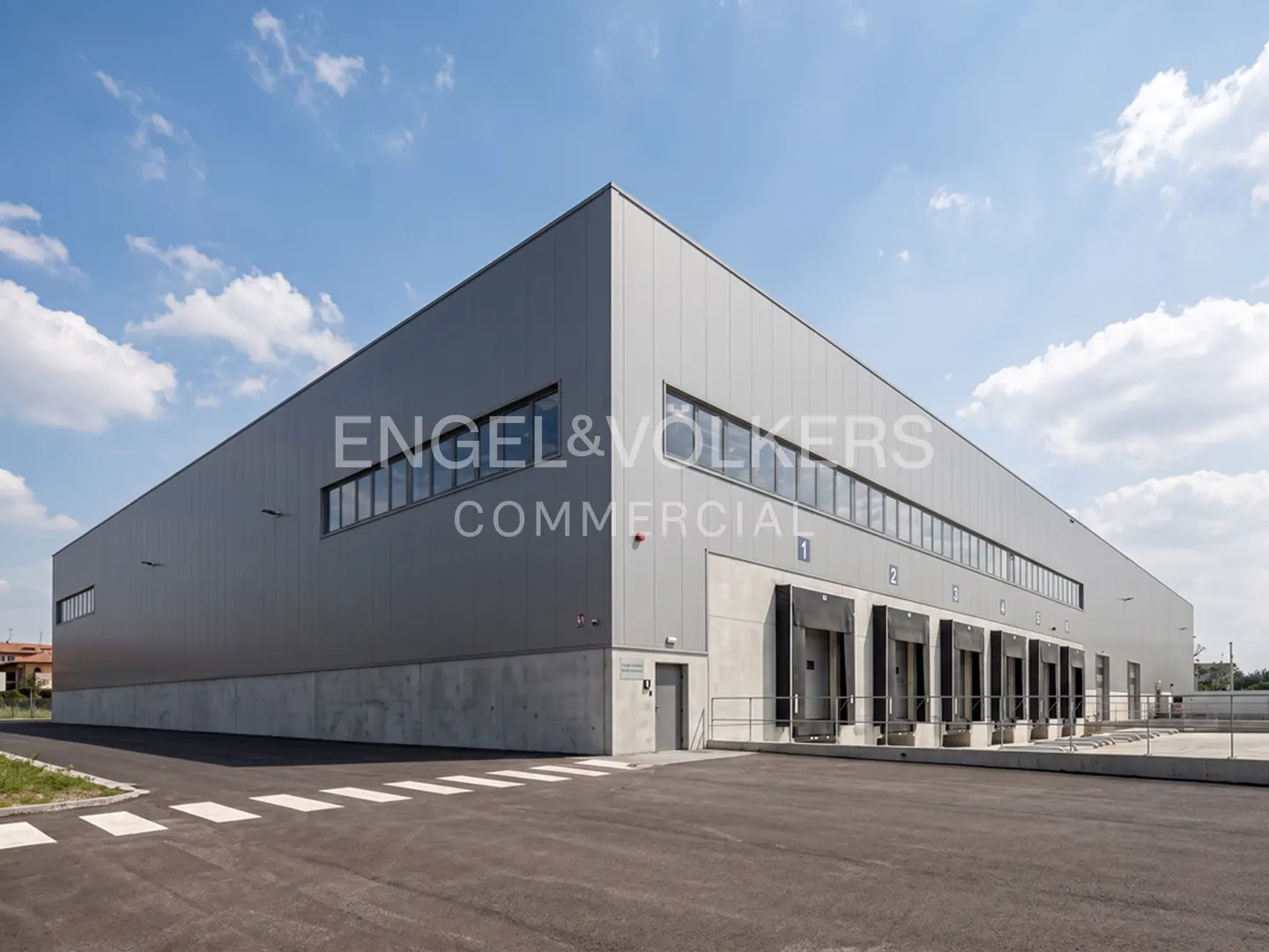 Exterior of a large, gray commercial building with loading docks under a blue, cloudy sky.