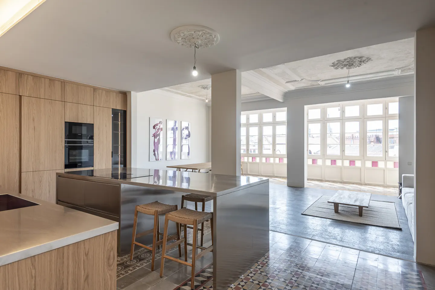 Open-concept kitchen and living room with wood cabinets, stainless steel island with stools, and large windows.