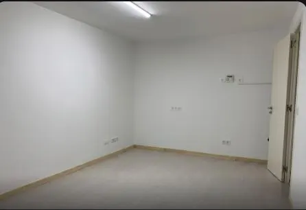 Empty room with white walls, light gray floor, and a white door slightly ajar on the right. A fluorescent light is on the ceiling.