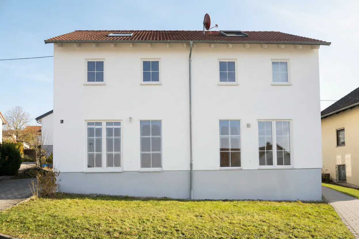 Two-story white house with a red tile roof, skylights, and a satellite dish. Green lawn in front.