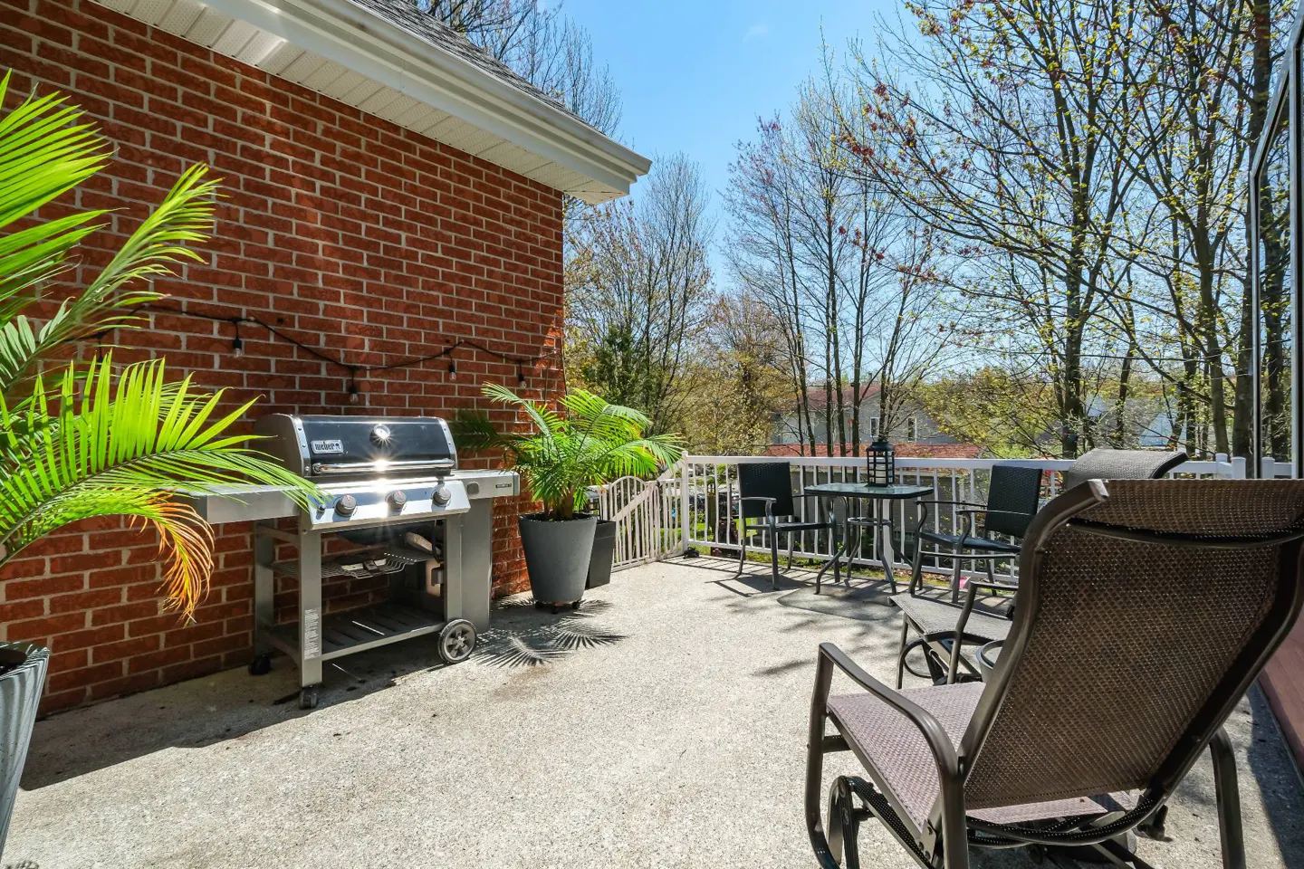 Outdoor patio with a grill, table, and chairs. A brick wall and potted plants add to the ambiance.