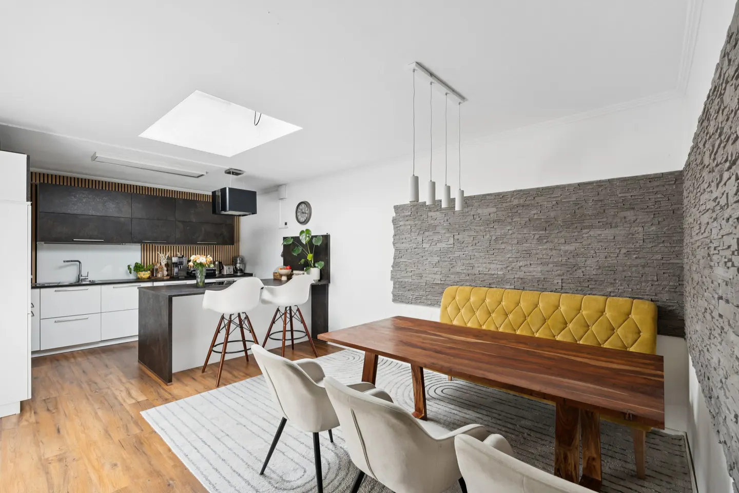 Modern kitchen with white and black cabinets, a wooden dining table, yellow tufted bench, and white chairs on a rug.