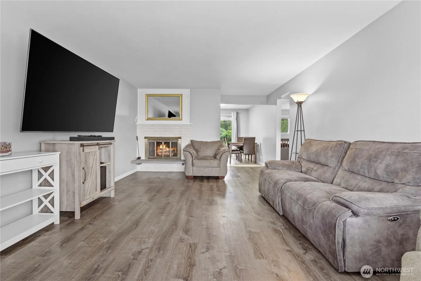 Living room with gray walls, wood floors, and a fireplace. A large TV is mounted above a cabinet. A gray sofa and chair are in the room.