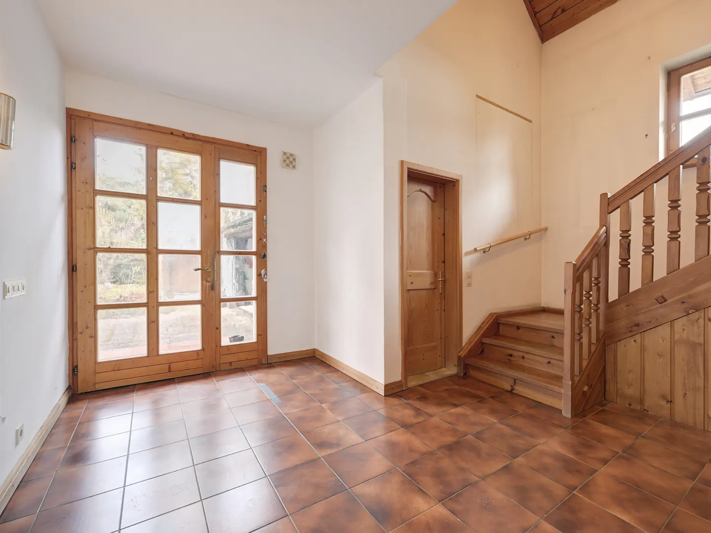 Foyer with brown tile floor, white walls, and wood accents. A glass paneled door is on the left, and a staircase is on the right.