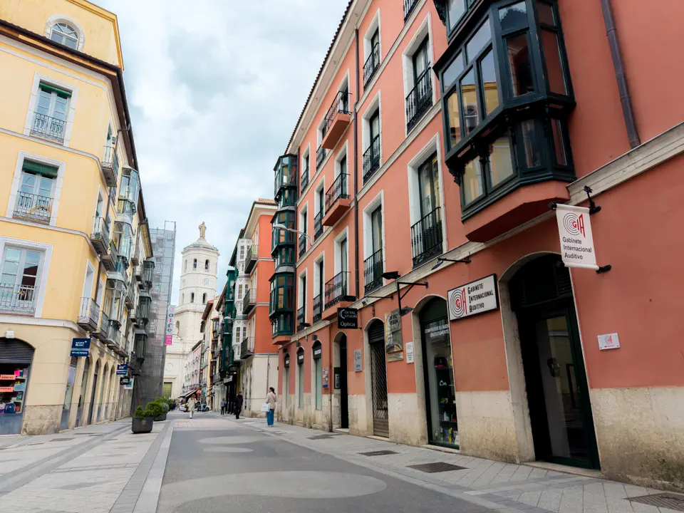 Street view of Valladolid, Spain, with yellow and pink buildings, balconies, shops, and a church tower in the background.