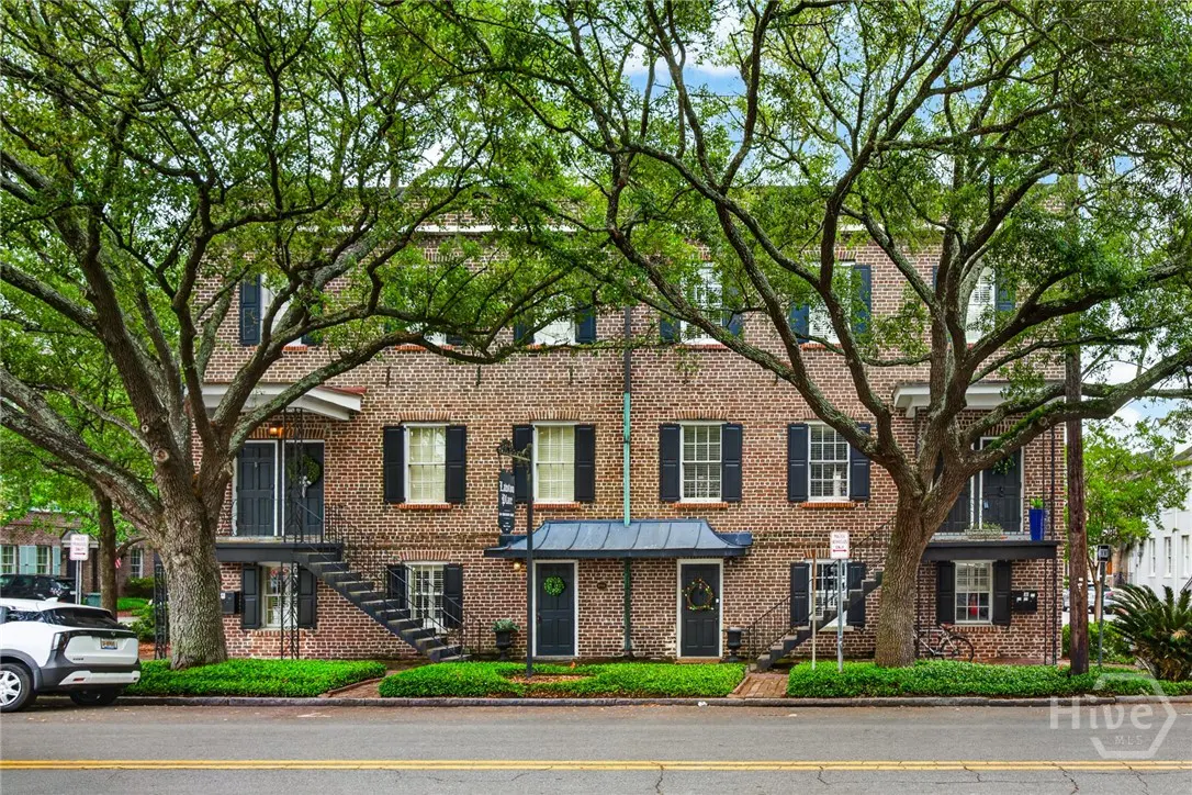 Brick apartment building with black shutters and doors, framed by large trees. A street runs in front of the building.