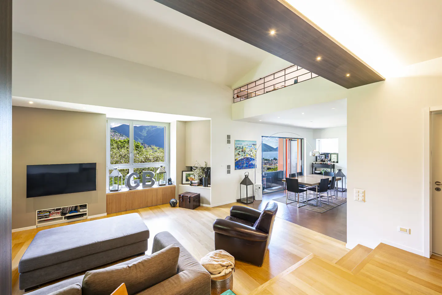 Bright, modern living room with hardwood floors, gray sofa, brown leather chair, and large window with mountain view.