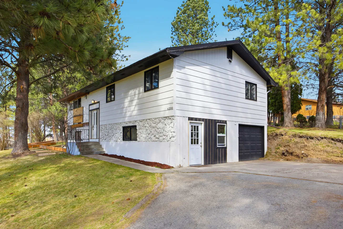 Two-story white house with black trim, a stone facade, and a black garage door. Trees surround the house.