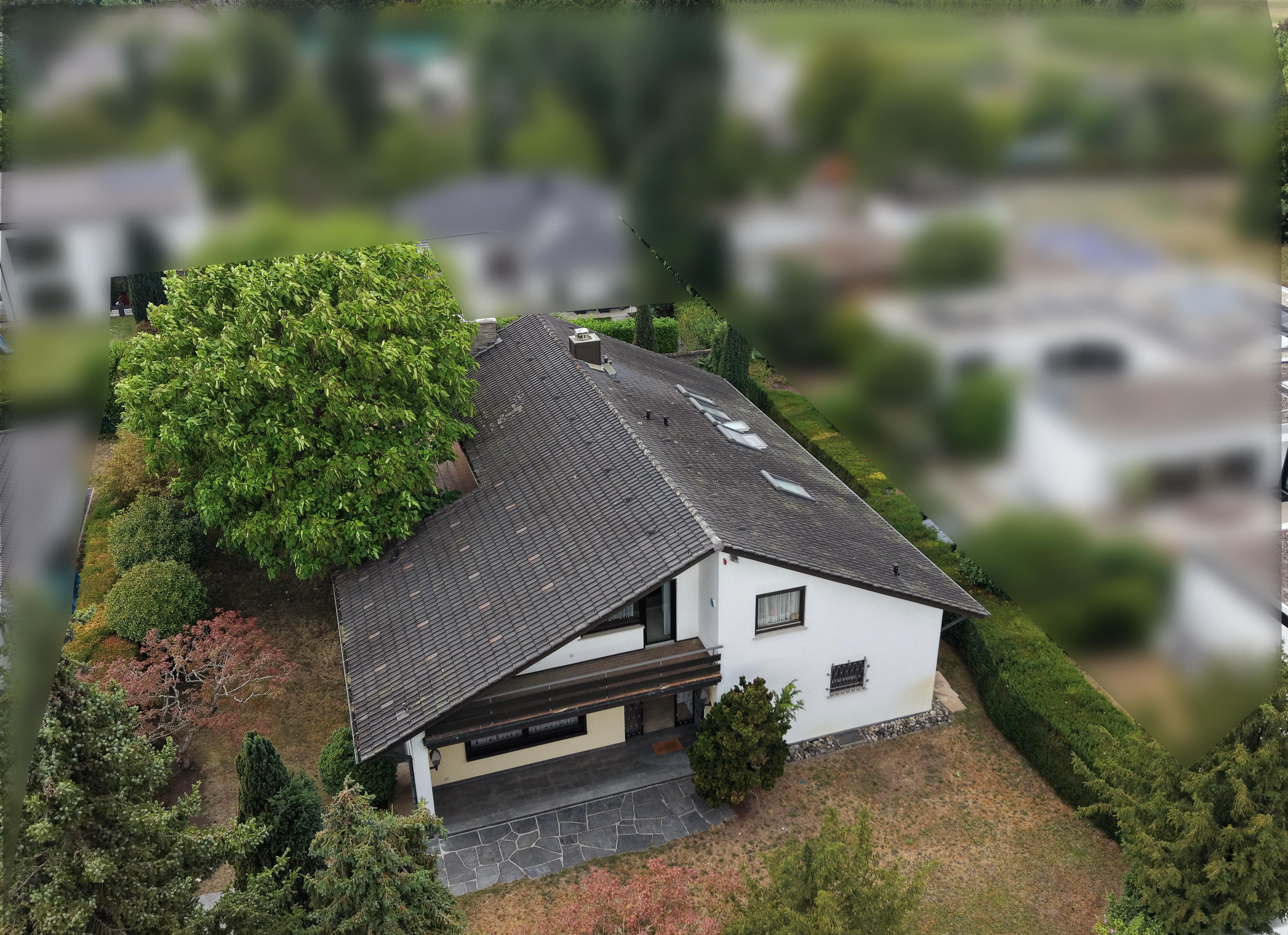 Aerial view of a white house with a dark tiled roof, surrounded by trees and a stone patio in a residential neighborhood. [AI-generated text]