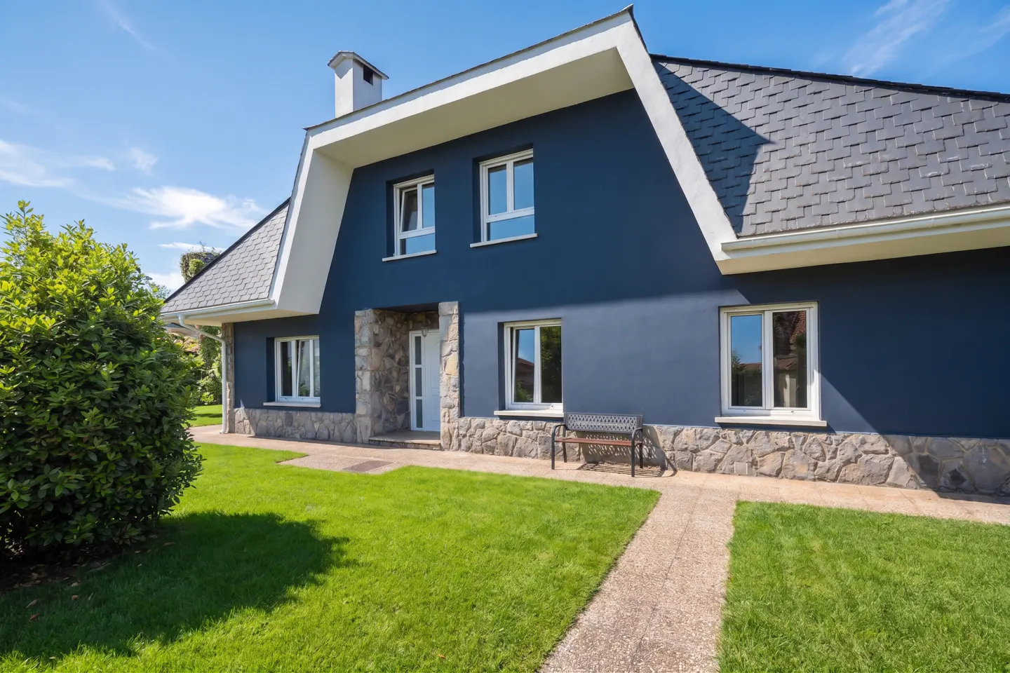 Two-story blue house with gray roof and white trim, stone accents, green lawn, and blue sky.
